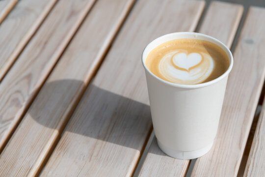 Warm latte with heart design on wooden table in sunny cafe setting