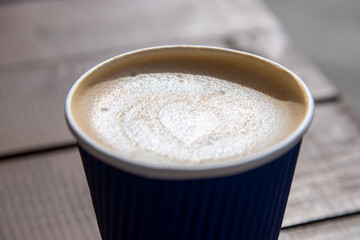 Delicious latte with a heart pattern served in a blue cup on a wooden table