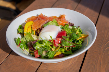 Fresh salad with smoked salmon and poached egg served outdoors on a sunny day