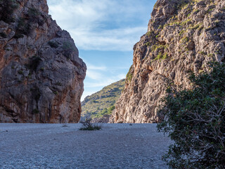 Sa Calobra beach Mallorca, serene canyon with towering rocky cliffs and sparse vegetation, framed by a clear blue sky, Majorca