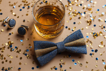 Bow tie, matching cufflinks, and glass of drink surrounded by confetti.
