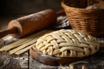 Unbaked pie with a woven lattice crust, rolling pin and basket nearby