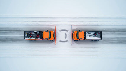 Top-down aerial view of snowplows clearing highway lanes, bright orange machines contrasting with white snow, geometric tire patterns, realistic winter work