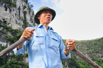 Local man wearing a hat guiding a boat through the iconic misty karst landscape and calm waters of ha long bay, offering a traditional travel experience