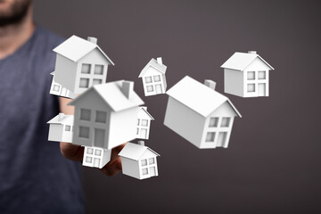 Conceptual image of a person's hand holding miniature houses, symbolizing home ownership, real...