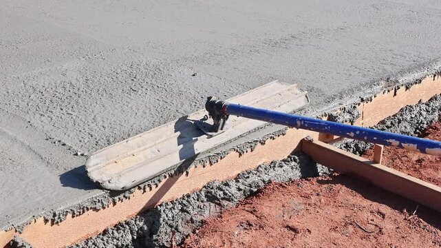 Construction worker uses leveling tool to smooth wet concrete on building site