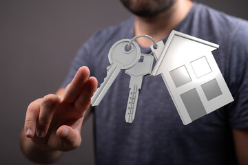 Conceptual image of a man holding keys with a house-shaped charm. Symbol of homeownership, buying, and real estate. Perfect for illustrating pro