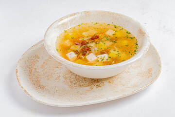 A bowl of Chicken Soup with potatoes, herbs, and dried tomatoes sits on a neutral plate