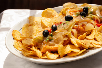The "Bacalhau com Cebolada", a traditional Portuguese dish made with fried codfish topped with sautéed onions, peppers, and olives, served with crispy round potato chips.