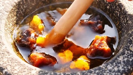 Mortar and pestle with amber-like materials in a liquid. A wooden piece stirring