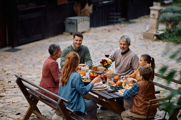 Happy multi-generation family gathering at dining table while celebrating Thanksgiving on patio.