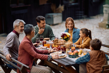 Happy multi-generation family talking while having Thanksgiving meal on patio.