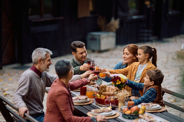 Happy extended family toasting while celebrating Thanksgiving together on patio.