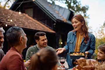 Happy woman talking to her extended family while serving food on Thanksgiving.