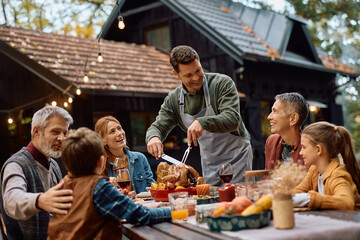 Happy man carving turkey meat during Thanksgiving meal with his extended family.