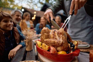 Close up of man carving turkey while having Thanksgiving meal with his extended family.