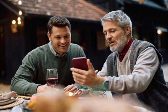 Mature man and his son using smart phone at dining table on patio.