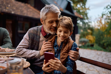Happy kid taking selfie with his grandfather while celebrating Thanksgiving on patio.