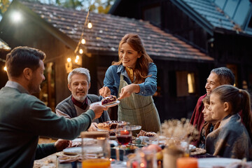 Happy woman serving sweet pie while celebrating Thanksgiving with her extended family.