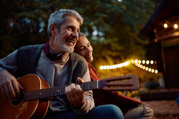 Romantic mature man playing acoustic guitar to his wine on autumn evening.