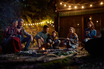 Obraz premium Happy extended family roasting corn on fire on autumn evening.