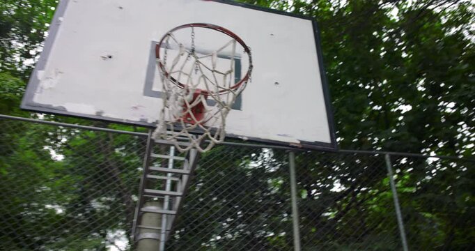 Hispanic man missing basketball shot during outdoor street game, handheld shot capturing failed throw toward hoop and quick reaction on urban court