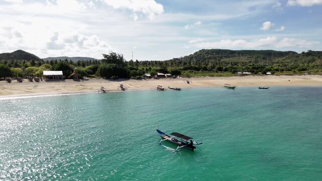 Aerial view of a traditional Indonesian outrigger boat floating on the calm turquoise sea near a beautiful sandy beach, showcasing a serene tropical island paradise on a sunny day