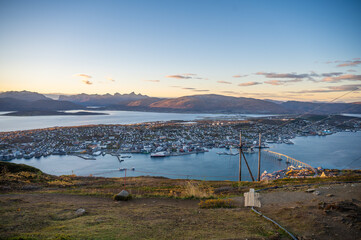 A panoramic view of Tromso, Norway with a harbor, surrounded by mountains and a bridge, set against a serene sky at sunset, at the top of Storsteinen