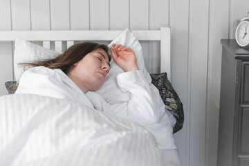 A woman is sleeping peacefully in her bed with a white pillow and a blanket. A beautiful young happy lady is sleeping peacefully on a cozy bed in the morning light at home, in a relaxed atmosphere