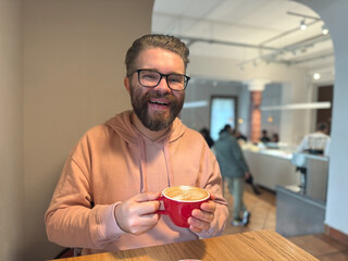 Man smiling with cup of coffee in modern cafe. Expression of joy, warmth and everyday connection over morning beverage.