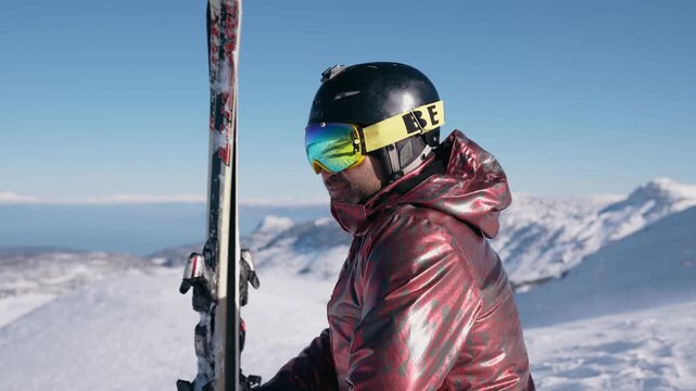 A skier standing on a snowy mountain peak holding skis upright, admiring the panoramic view. A winter sports scene full of freedom, adventure, and nature.