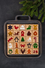 Advent Calendar. 25 festive square cookies with colored curly marmalade filling. On a wooden plate. Dark background. Top view