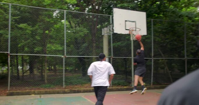 Teammates passing basketball and attempting to score but missing the hoop during outdoor street game, handheld camera captures motion, teamwork, and frustration