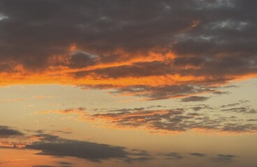 Orange sunset clouds over calm sky. Warm evening light with golden and violet tones. Atmospheric cloudscape capturing natural beauty and colour gradient.