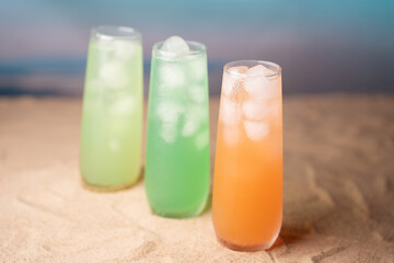 vibrant trio of refreshing drinks in tall glasses on sandy surface with blurred beach horizon and sky, capturing a breezy summer atmosphere and tropical vibes, flavors, decor, minimal, smooth