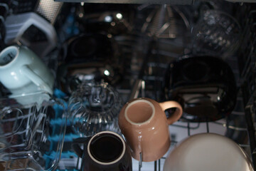 a collection of assorted ceramic and glass mugs, bowls, and cups neatly arranged in a dishwasher's dark interior, emphasizing reflections and subtle play of light on the surfaces, intimate, compact