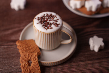 cozy scene featuring latte with chocolate sprinkles in a ribbed mug, paired with decorative biscuits on a saucer, on a dark wooden table, creating a warm and inviting atmosphere, textured, brownies