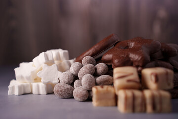assorted chocolates and sweets on soft gray surface with brown background, featuring white marshmallows, chocolate-coated biscuits, and confectionery candies in a cozy setting, comfort, pleasure