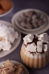 aesthetic dessert arrangement featuring creamy mousse garnished with whipped cream, marshmallows, chocolate shavings, and pralines on neutral plates for a cozy indulgence, elegance, simplicity