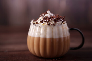 delicious coffee topped with whipped cream and chocolate sprinkles served in a textured glass mug on a wooden surface, evoking a cozy, indulgent atmosphere in warm tones, toppings, aroma, sugar
