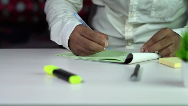 Man Sitting at Desk in Office Diligently writing on Notebook.