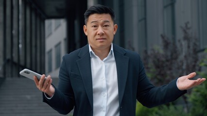 Asian businessman in city confused with mobile problem Korean business man shrug shoulders with...