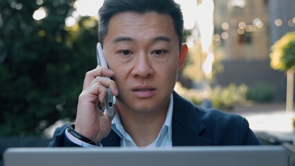 Serious Asian business man talking mobile phone laptop using looking computer Korean businessman...