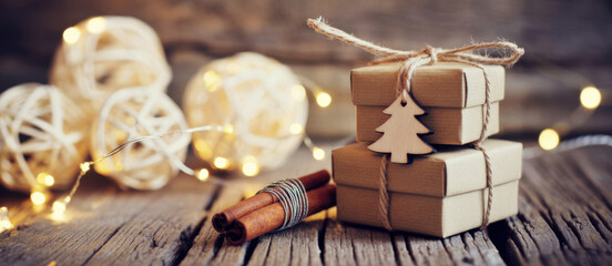 Rustic Christmas gifts with cinnamon sticks and string lights stacked on wooden surface holiday season concept