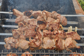 Large pieces of pork being grilled on skewers over hot charcoal. Delicious barbecue with a golden crust cooking outdoors during a picnic or countryside gathering.