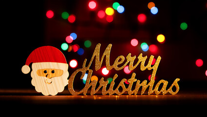 Wooden Santa Claus decoration with golden glitter text against bokeh lights christmas