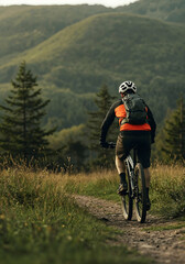 Naklejka premium Adventure on the Trail: A lone mountain biker embarks on a scenic journey, navigating a rugged trail, with lush hills and vibrant nature embracing the thrill of the ride.