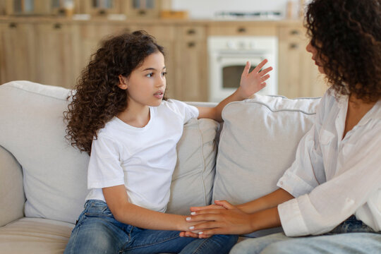 Thoughtful preteen girl talking with her mother, mum consoling daughter, giving support, touching hand of child, sitting together on sofa at home