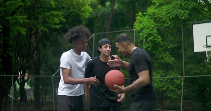 Three young men greeting each other with friendly handshake on outdoor basketball court, smiling and bonding before game, expressing camaraderie and urban friendship