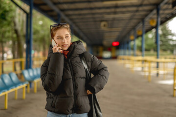 Fototapeta premium Girl Talking On Phone In Spring While Waiting For A Bus At The Bus Station